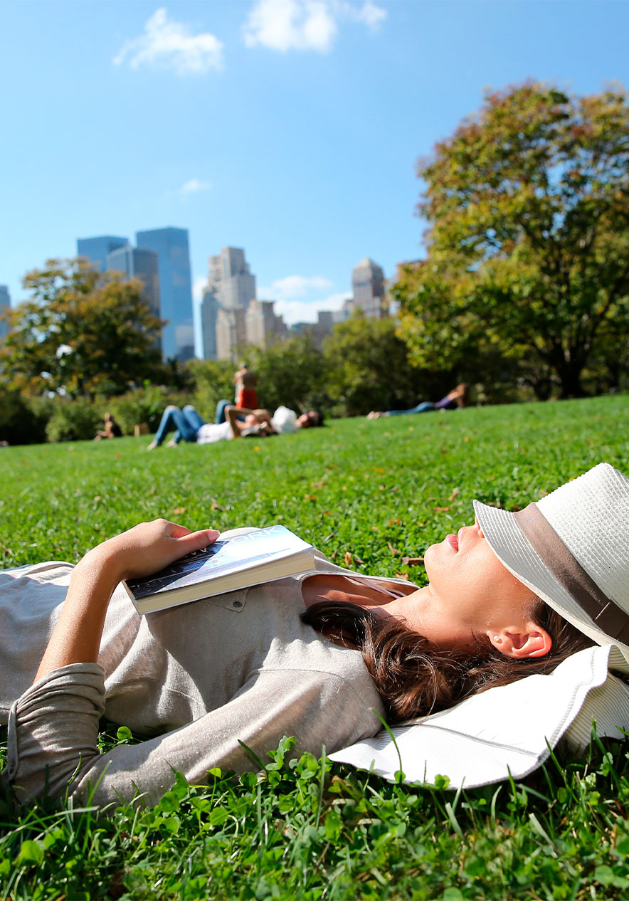 Vista panorâmica do Central Park, com o horizonte de Manhattan ao fundo, com pessoas a descansarem na relva do parque