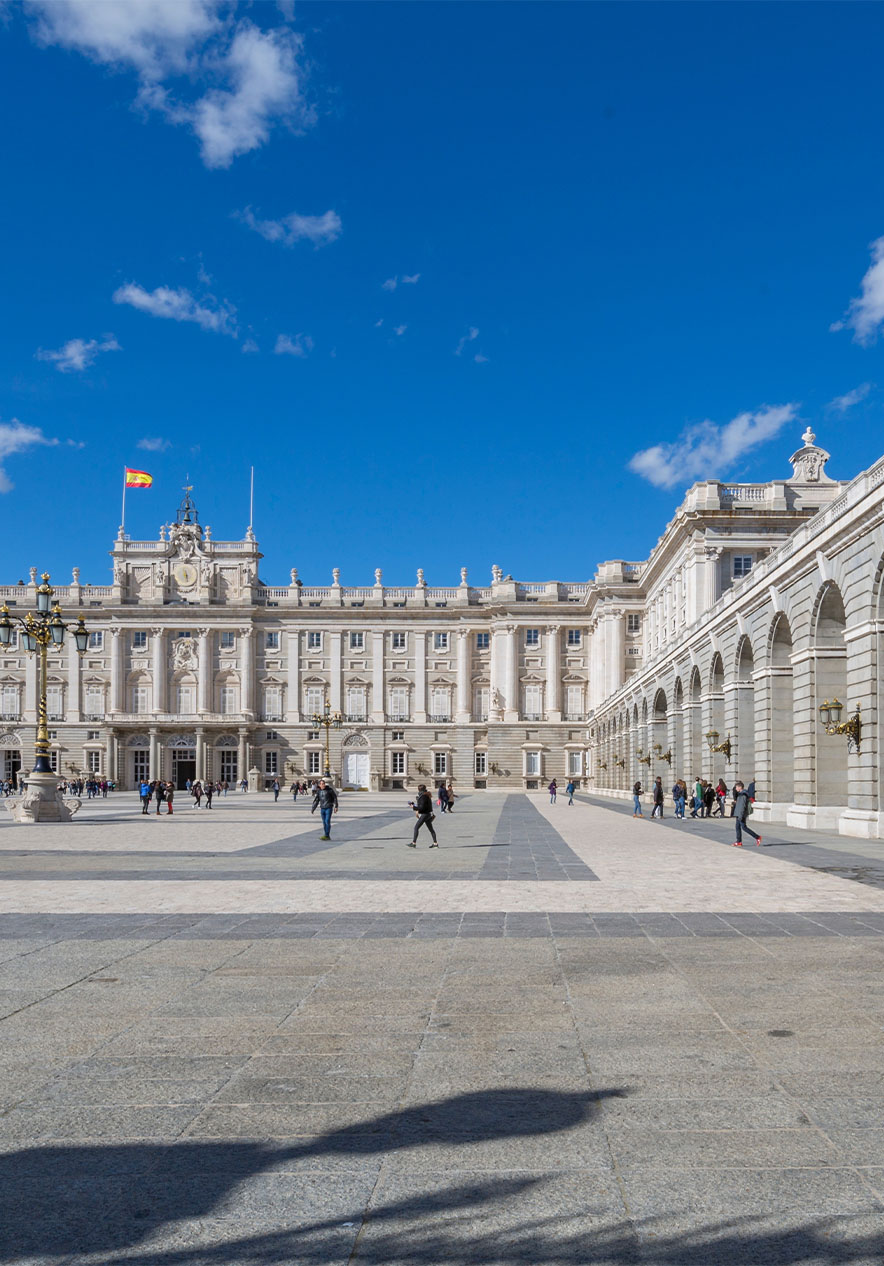 Pátio do Palácio Real, com os edifícios de pedra em redor, formando um quadrado com pessoas e a bandeira de Espanha 
