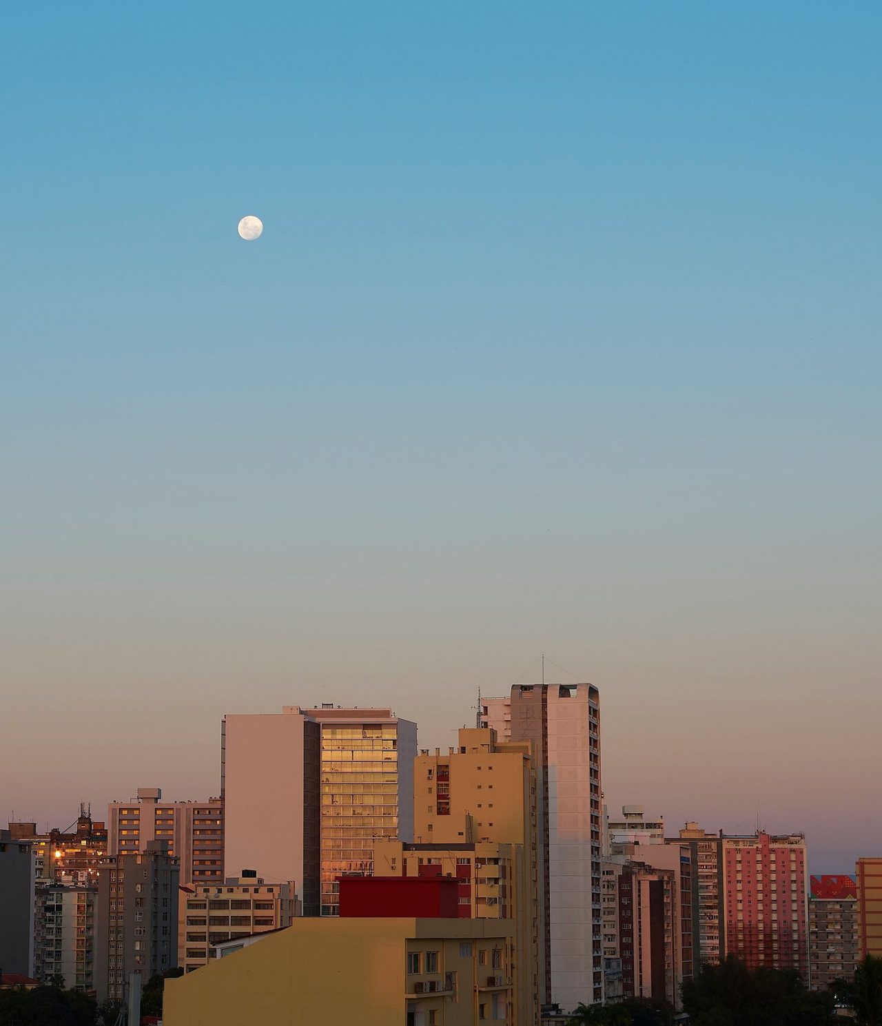 Top view of several buildings in Maputo, with dusk light on them and the moon high in the sky