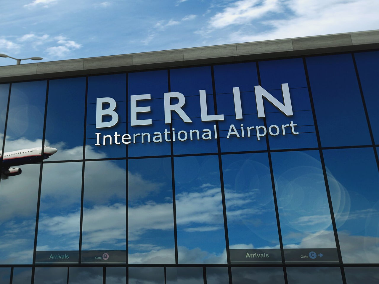 Facade of the arrivals area of Berlin International Airport, with a plane reflected in the windows