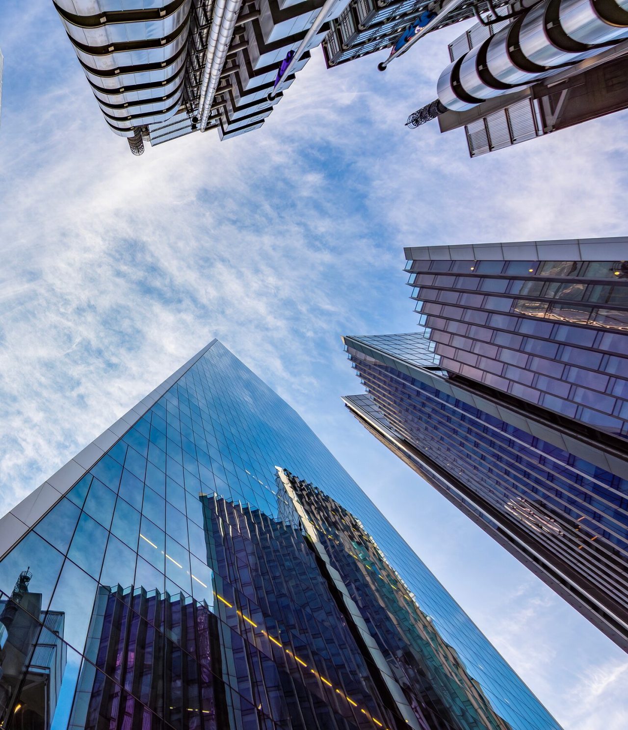 View from below of the famous modern tall buildings in London, with many windows and a blue sky behind