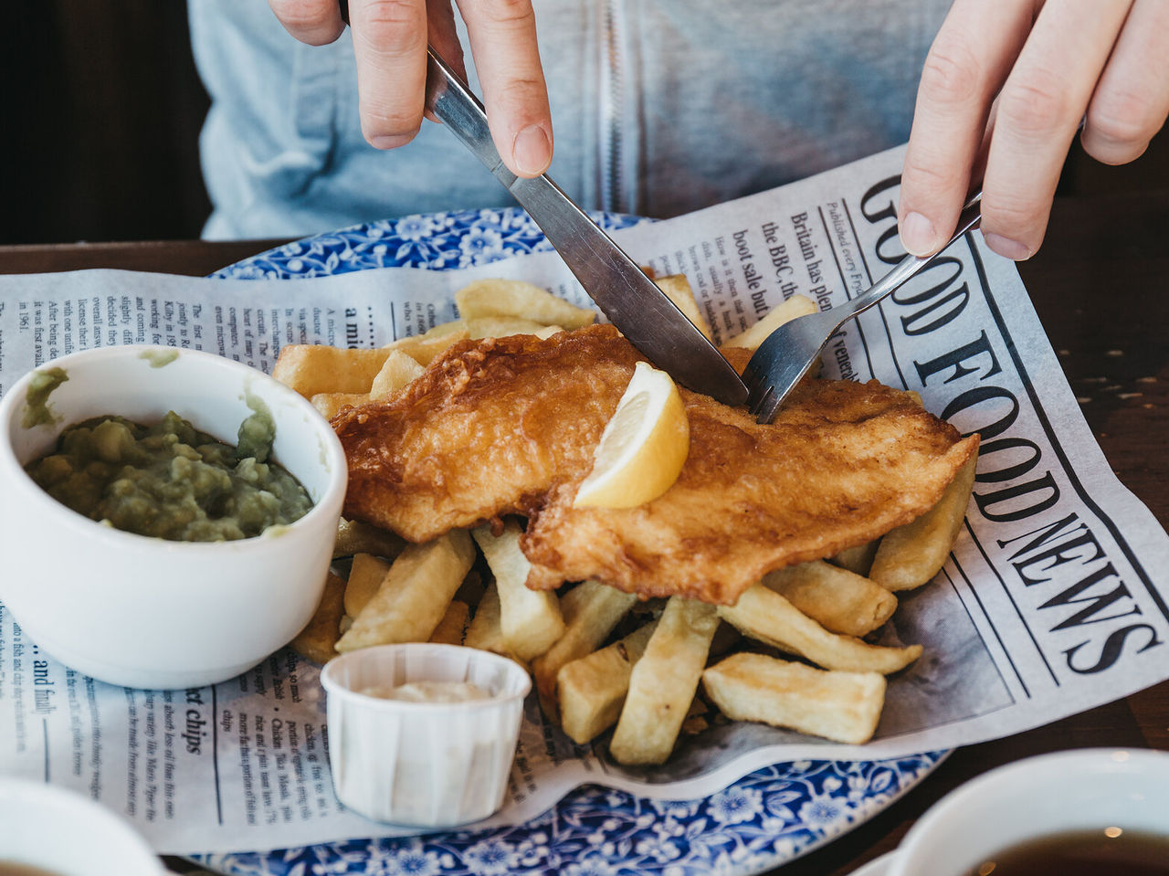 A person enjoying a typical English dish of fish and chips, consisting of fried fish served with crispy chips