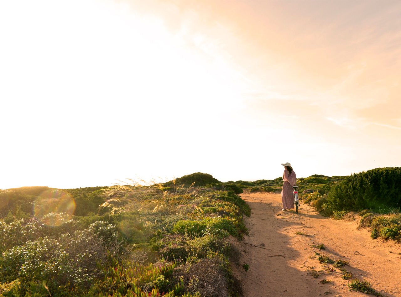 Woman cycling on a dirt road through the dunes, with a bicycle from Pousadas de Portugal